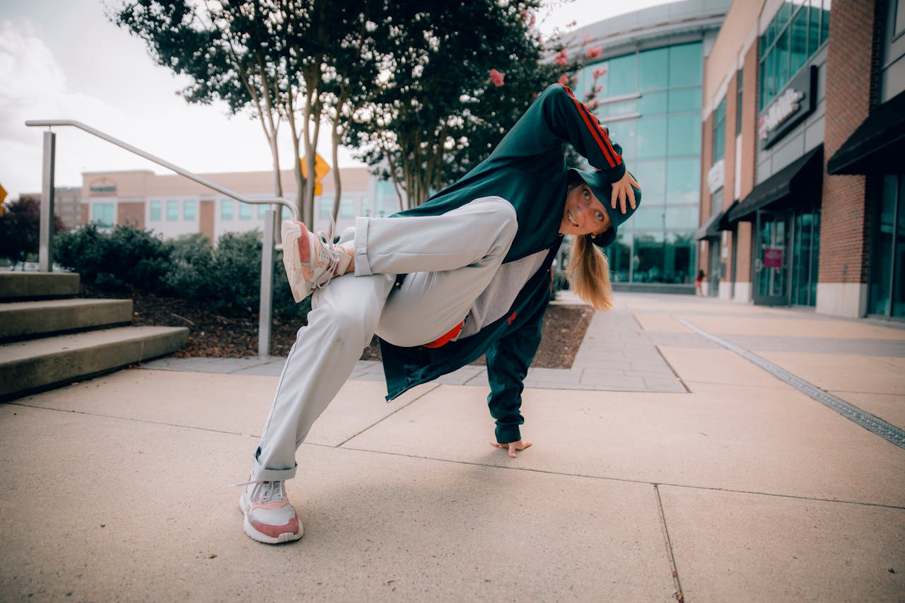 A woman performing a breakdancing move on a city sidewalk in casual attire.